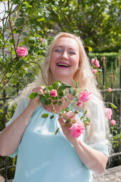 Preview: Middle-aged caucasian woman with long blond hair laughs against the background of a rose bush
