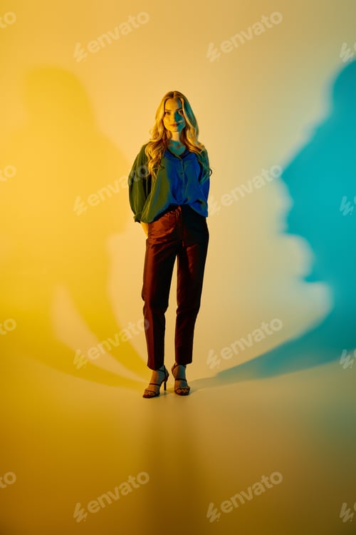 Preview: Young stylish woman showcases vibrant fashion in colorful light setting for modern aesthetic