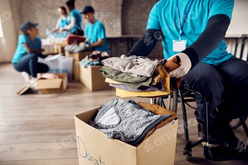 Preview: Close up of man in wheelchair packs clothing in donation box while volunteering at community center.