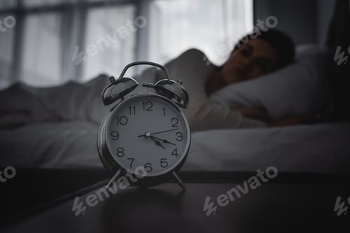 Preview: selective focus of alarm clock on bedside table near awake woman
