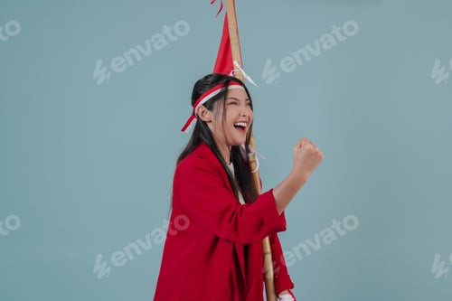 Preview: Close up portrait of Indonesian woman wearing red jacket holding a flag while raising fist gesture.
