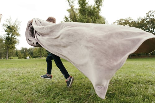 Preview: Cheerful boy running with a flying blanket in the park