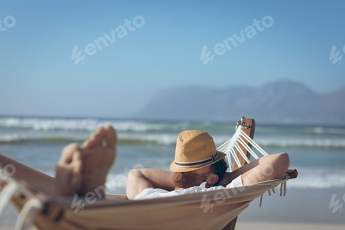 Preview: Front view of young Caucasian man relaxing on hammock at beach on a sunny day
