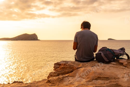 Preview: A tourist sitting watching the sunset at Cala Comte beach on the island of Ibiza. Balearic