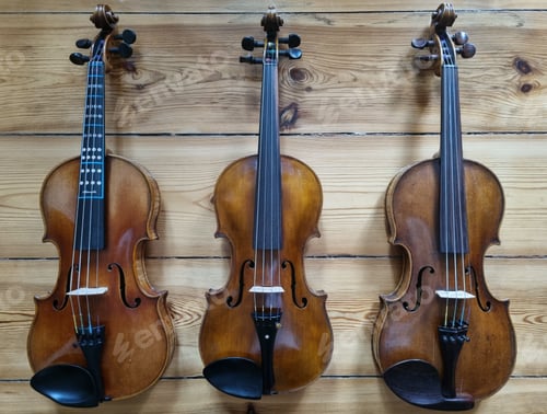 Preview: Three violins hanging on a wooden wall.