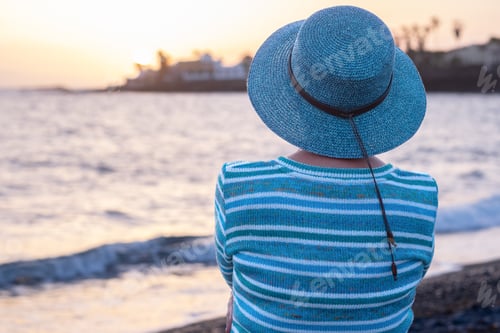 Preview: Rear view of relaxed caucasian senior woman sitting on the beach enjoying the golden hour of sunset