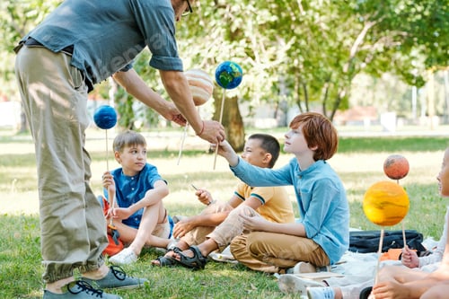 Preview: Teacher giving planet models to pupils
