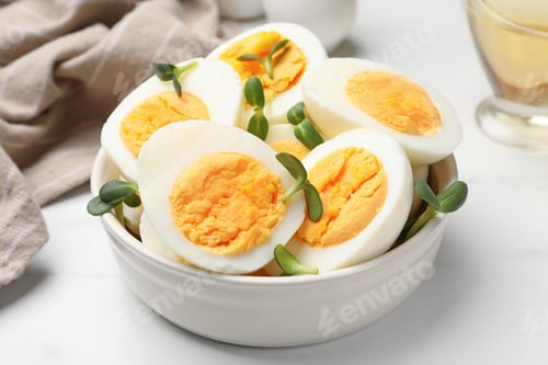 Preview: Halves of hard boiled eggs with microgreens on white table, closeup