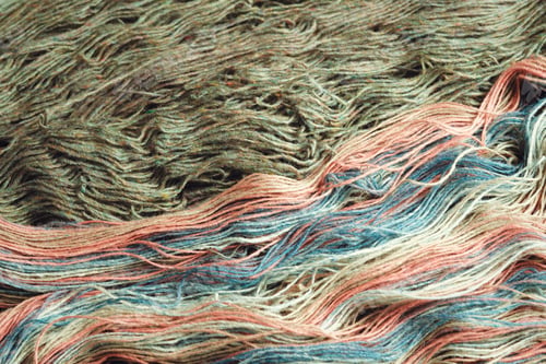 Preview: Threads from natural organic sheep wool. Two unwound skeins of green and rainbow knitting yarn.