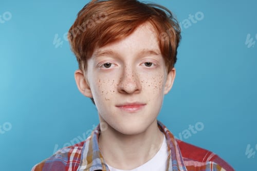 Preview: Cute teenage boy with freckles on light blue background, closeup