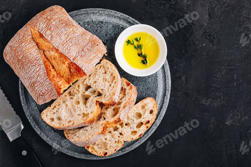 Preview: Italian ciabatta bread slices with olive oil on stone plate on dark concrete background