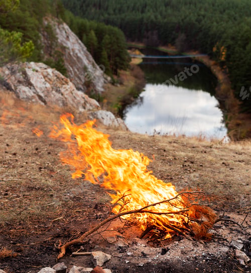 Preview: Bonfire burning against the background of river, cliffs and coniferous forest in autumn Landscape