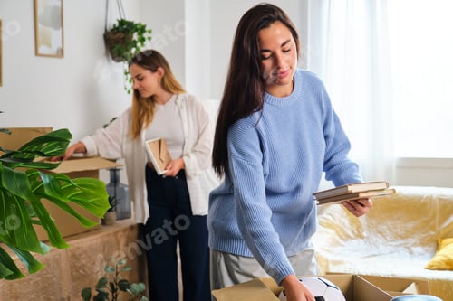 Preview: Two women packing in a moving cardboard box to settle in a new home.