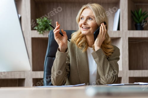 Preview: Beautiful mature adult businesswoman sitting at computer desk in the office