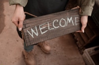 Preview: Woman Holds Rustic Welcome Sign Outdoors