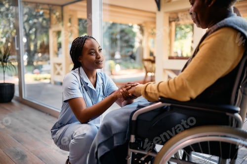 Preview: Caring black nurse comforting senior man in wheelchair at nursing home.