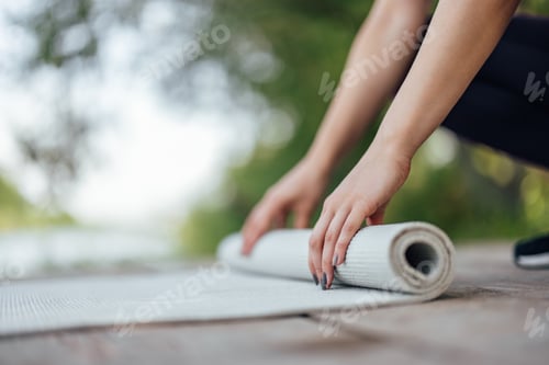 Preview: Woman Unrolling Yoga Mat Outdoors in Green Setting
