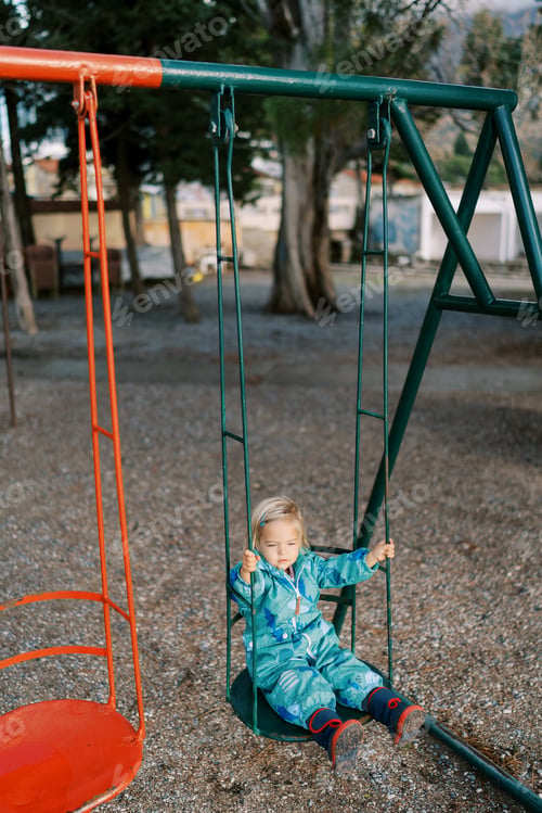 Preview: Little girl in overalls rides on a swing in the park