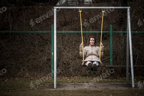 Preview: Smiling woman swinging on a swing in a park