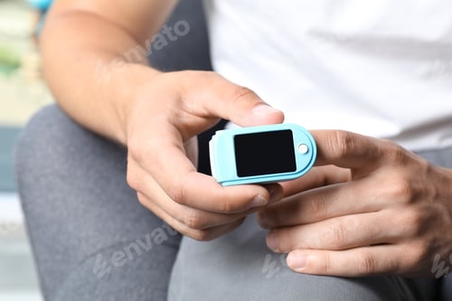 Preview: Young man checking pulse with blood pressure monitor on finger, closeup