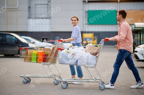 Preview: Cheerful couple with bags in carts on parking