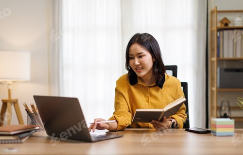 Preview: Young Asian woman smiling and focused, managing her work