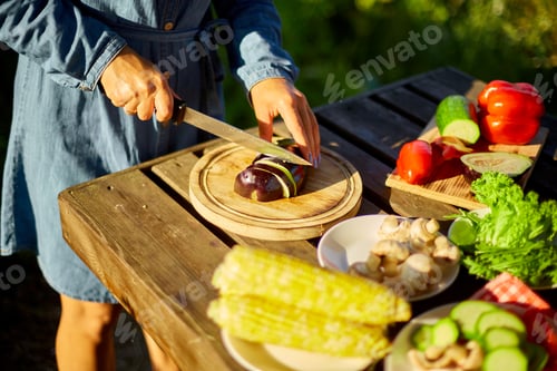 Preview: Unrecognizable woman cutting fresh eggplant vegetables on wooden board