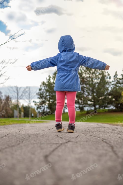Preview: Little girl standing on a road in the park in spring. Child from behind.