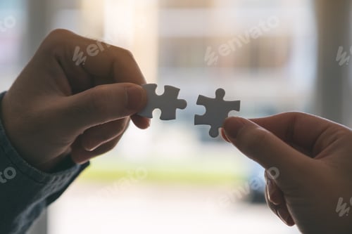 Preview: Closeup image of two hands holding and putting a piece of white jigsaw puzzle together