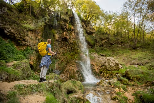Preview: Young hiker stopped beside a mountain waterfall to rest