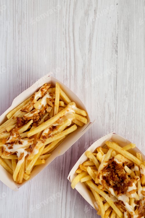 Preview: French fries with cheese sauce and fried onion in a paper box on a white wooden surface