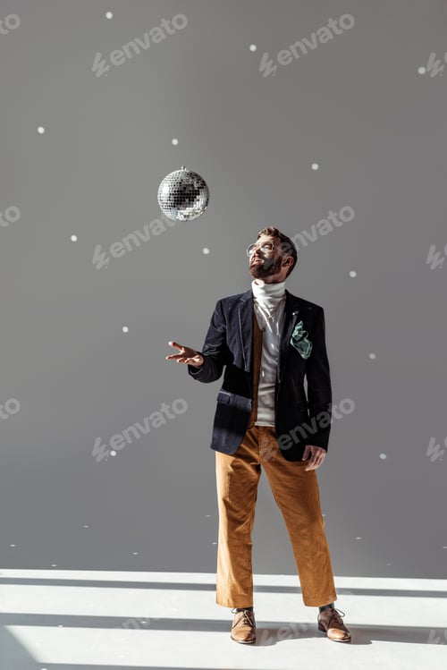 Preview: handsome man in glasses high throwing up disco ball on grey background