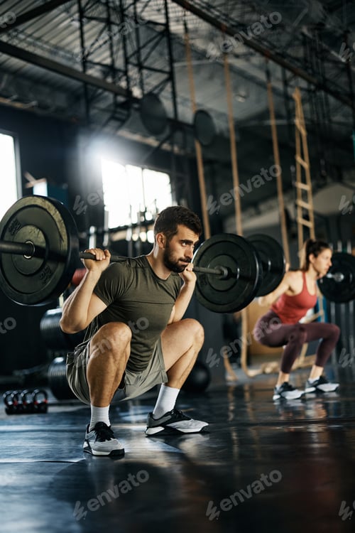 Preview: Athletic man using barbell while practicing squats during cross training in a gym.