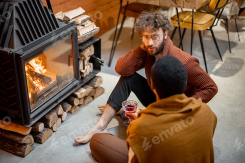 Preview: Two men sitting together by the burning fireplace at cozy home