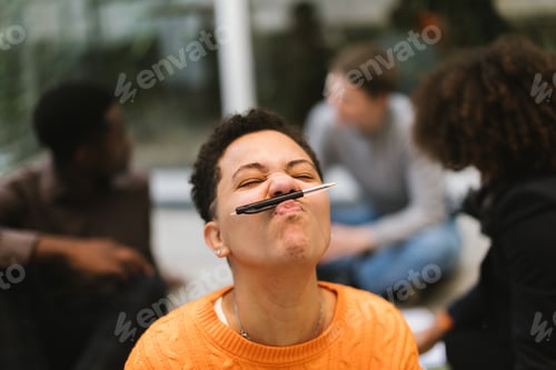 Preview: Playful student holding pen under nose making funny face during break