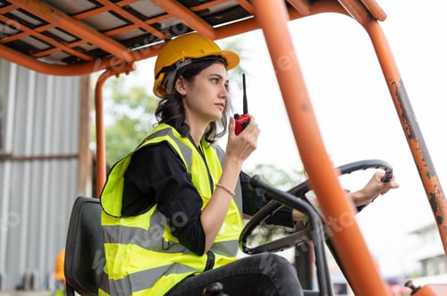 Preview: Female worker driving forklift truck using walkie talkie in factory