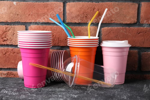 Preview: Set of disposable plastic dishware on grey textured table against brick wall