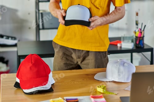 Preview: Cropped view of young craftsman holding snapback while working near tape measure and blurred laptop