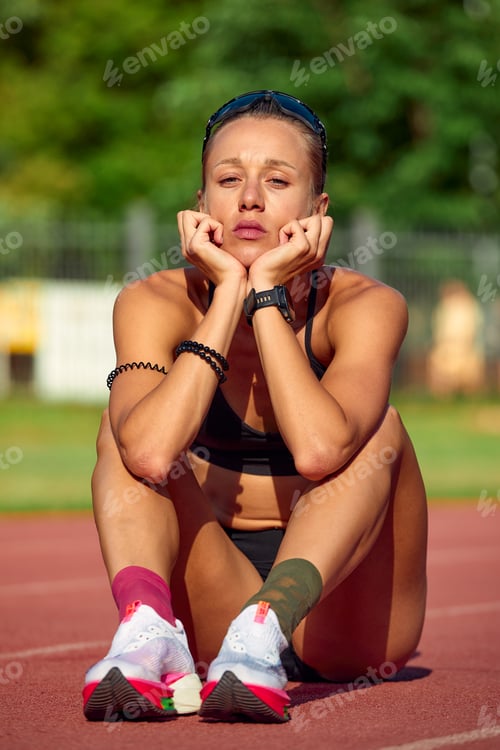 Preview: Fit woman in sportswear resting after training or running, sitting on a rubber treadmill, taking a