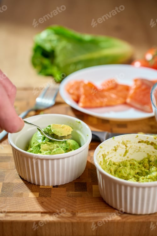 Preview: Hand mashing avocado in ramekin on cutting board with salmon