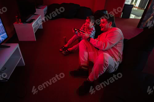 Preview: Father and son play gamepad video game console in red gaming room. Dad and kid gamers.