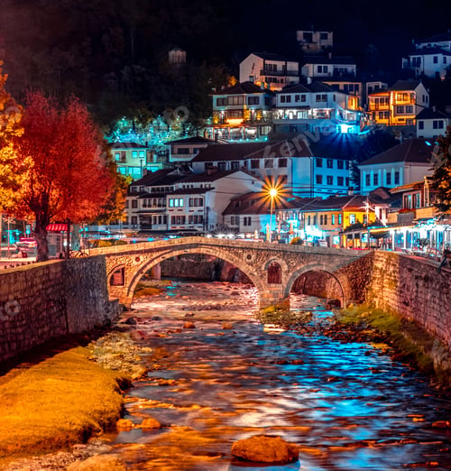 Preview: River with a stone bridge in downtown Prizren with buildings and trees at night, Pristina Kosovo