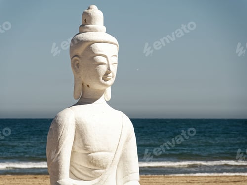 Preview: White Buddha statue on a sandy beach with the ocean in the background under a blue sky