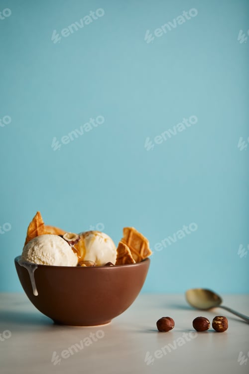 Preview: bowl of delicious scoops of ice cream with pieces of waffle on blue with copy space