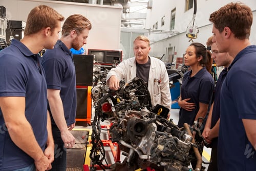 Preview: Mechanic showing parts of an engine to apprentices, close up