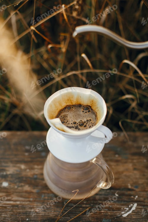 Preview: Hand pouring hot water from steel kettle in glass flask dripper with filter