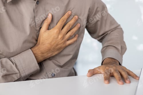 Preview: Man experiencing chest pain while touching his chest and resting hand on a table