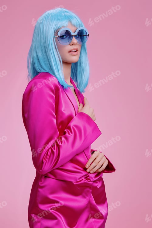 Preview: Woman in a pink suit, with blue hair and blue sunglasses, standing against a pink background