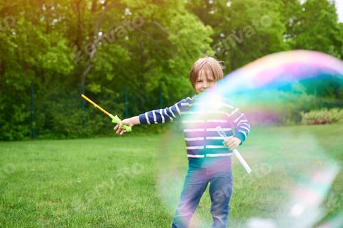 Preview: Outdoors portrait of cute preschool boy blowing soap bubbles on a green lawn at the playground.