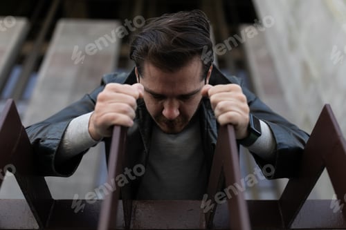 Preview: young caucasian man in depression stuck his head between the bars and looks down